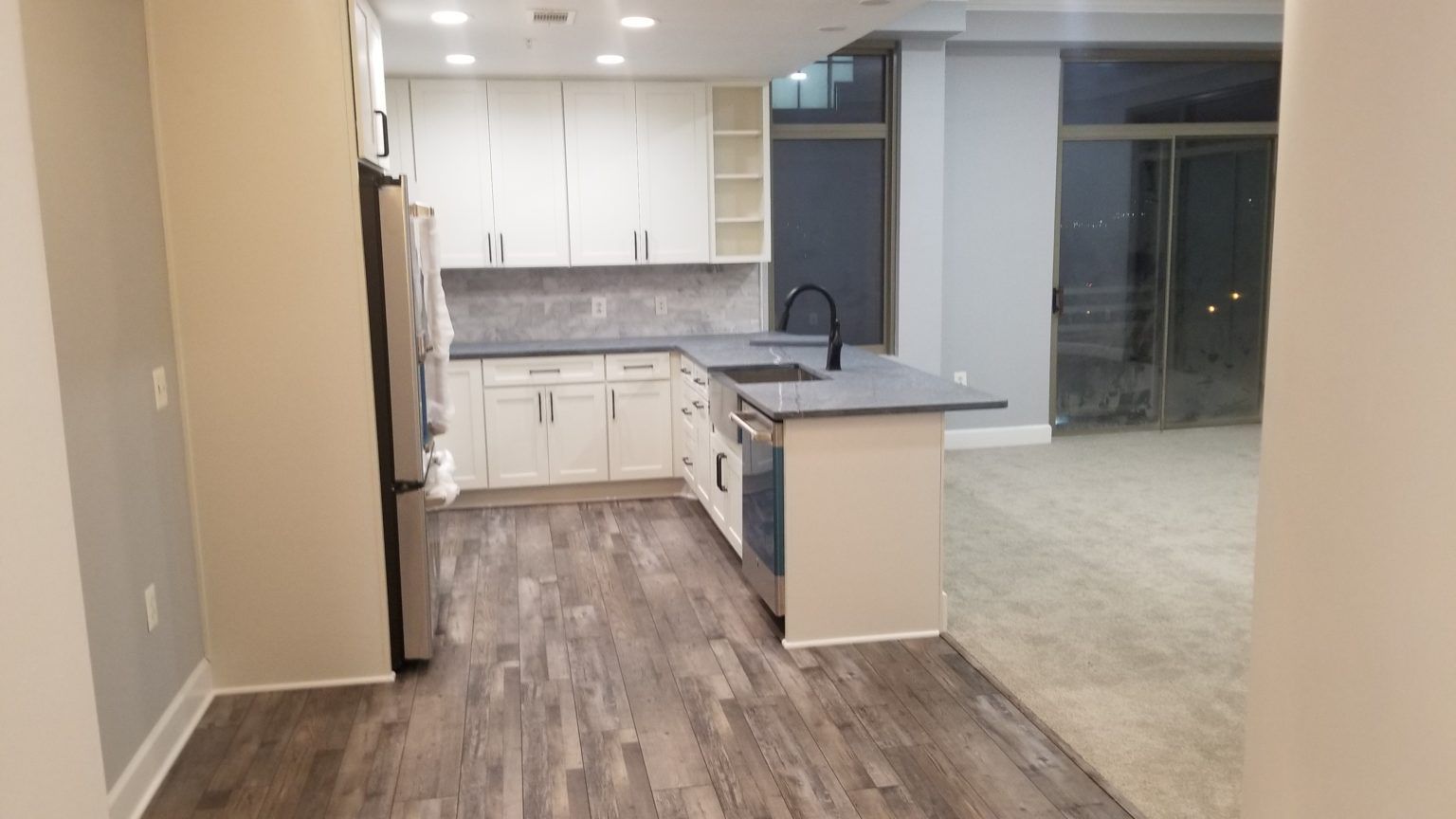 Kitchen with white cabinets, gray countertop, stainless steel appliances, and wood-look flooring.