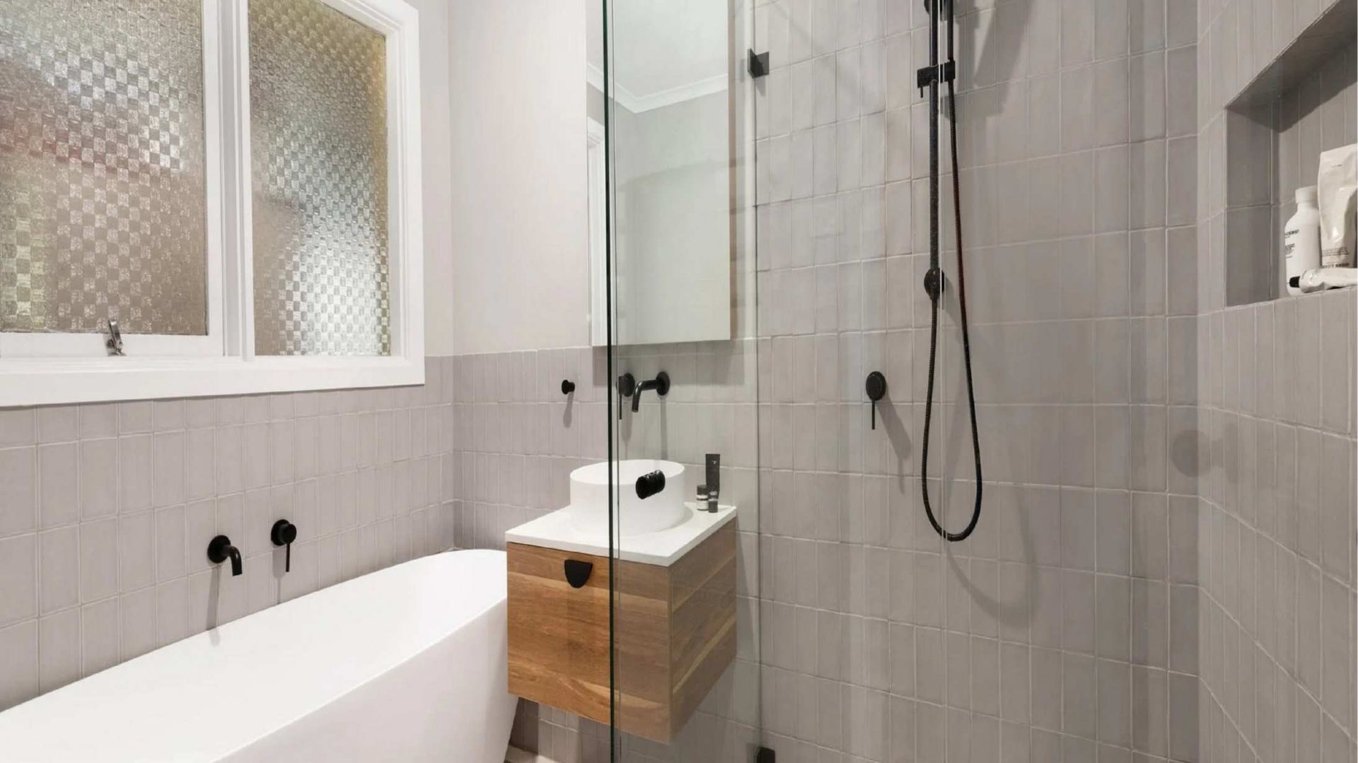Modern bathroom with grey tile, a white bathtub, and a wood vanity.