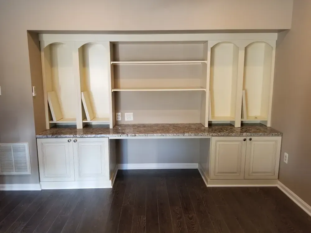 Built-in office space with cream-colored cabinets, granite countertop, and dark wood floor.