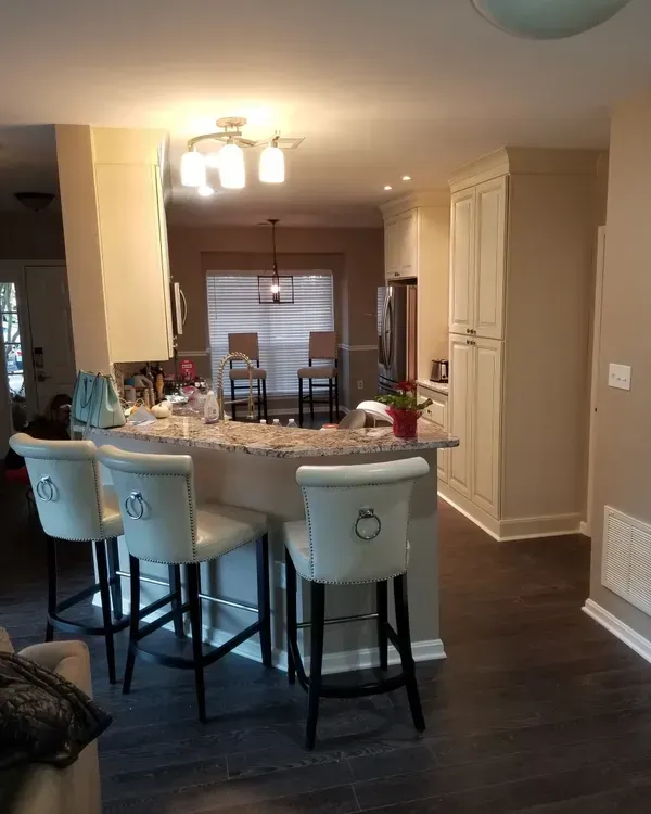 Kitchen interior with island, bar stools, cabinets, and dark flooring.