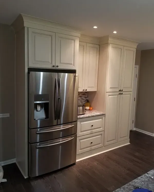 Stainless steel refrigerator built into cream-colored kitchen cabinets. Dark wood floors.