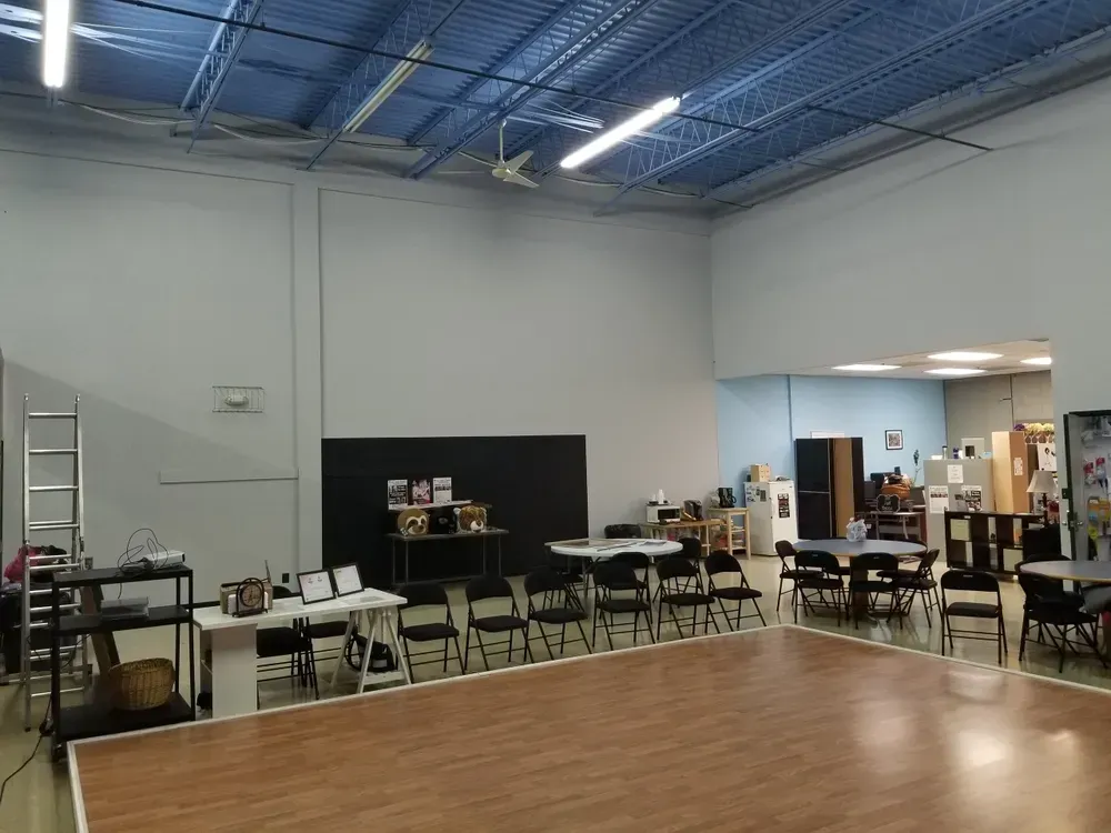 Large room with a dance floor, tables, chairs, and a small stage; light blue walls and ceiling.