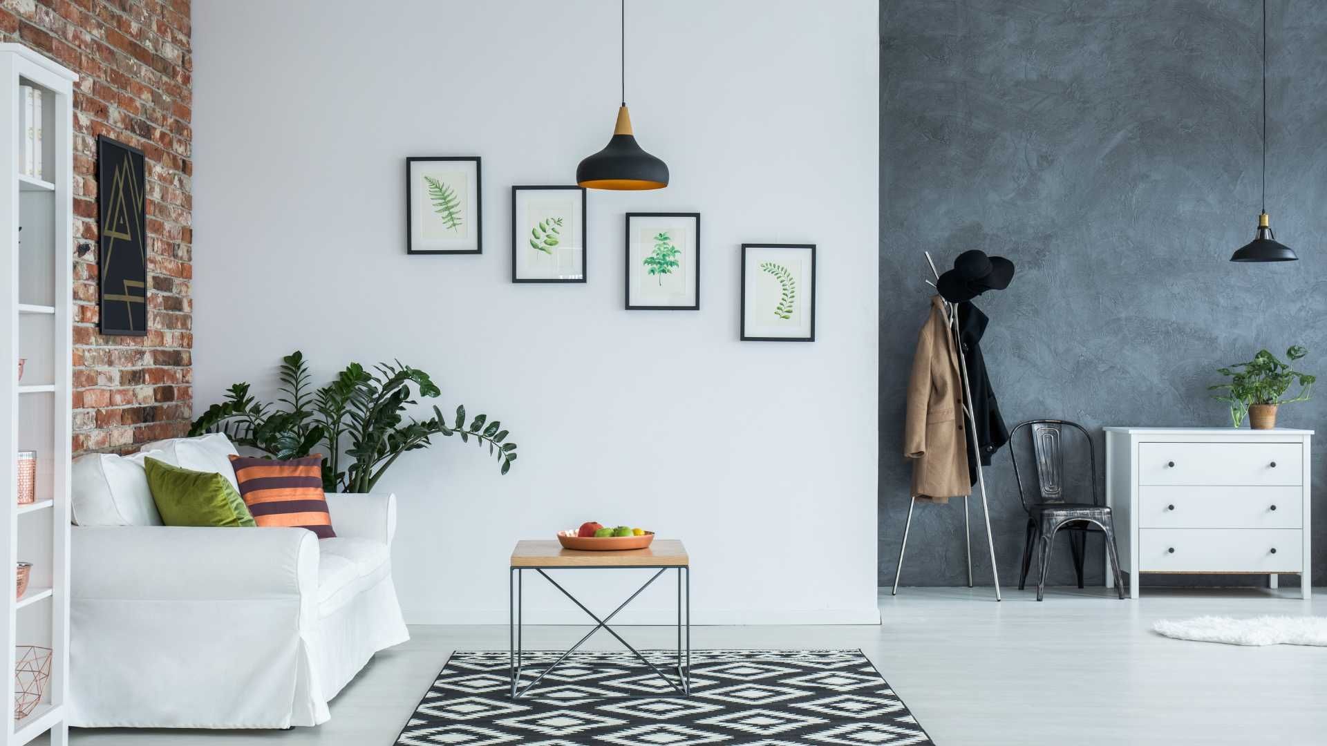 A modern living space with white couch, brick wall, artwork, and a patterned rug.