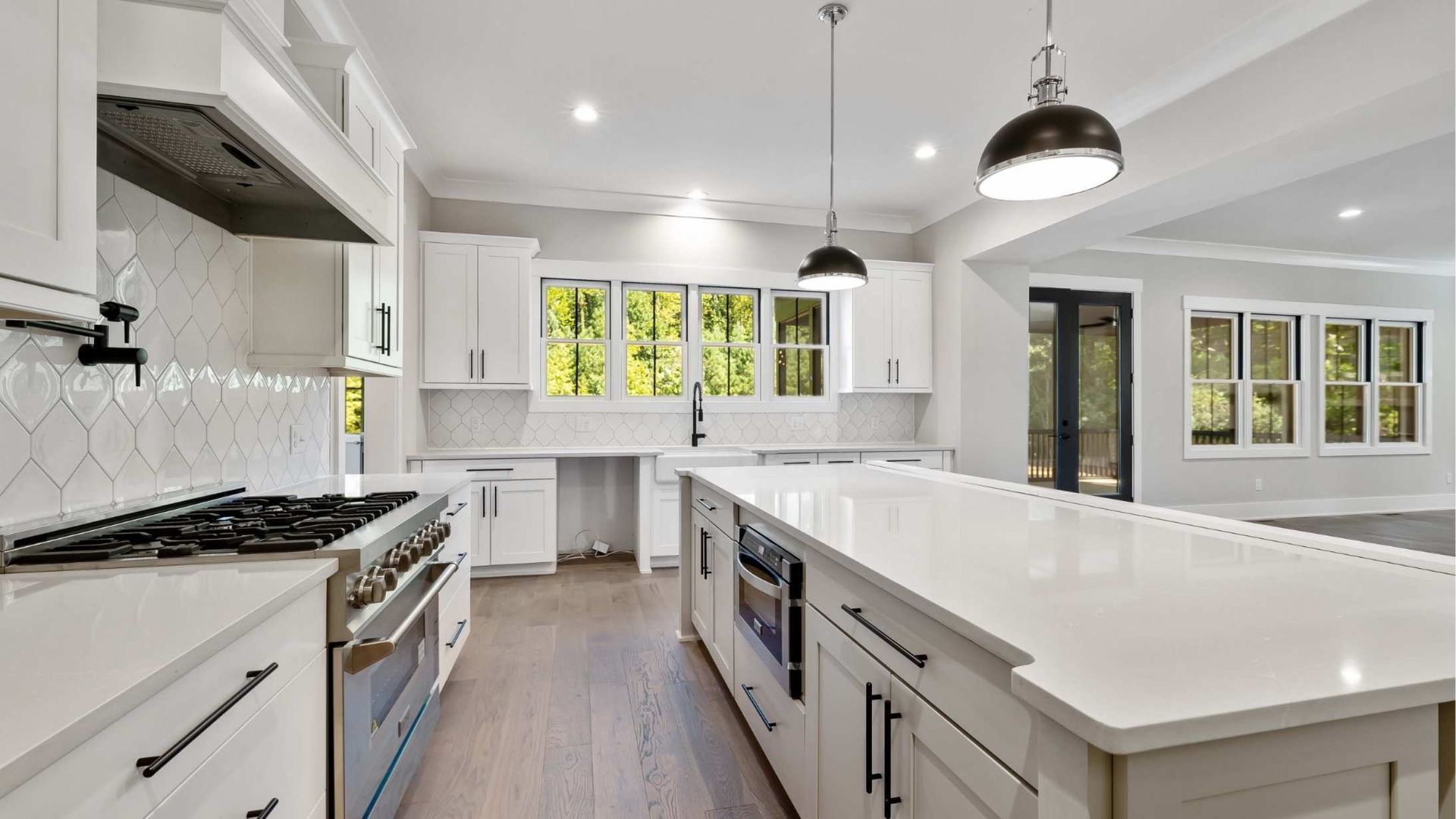 Modern white kitchen with island, range, and windows.