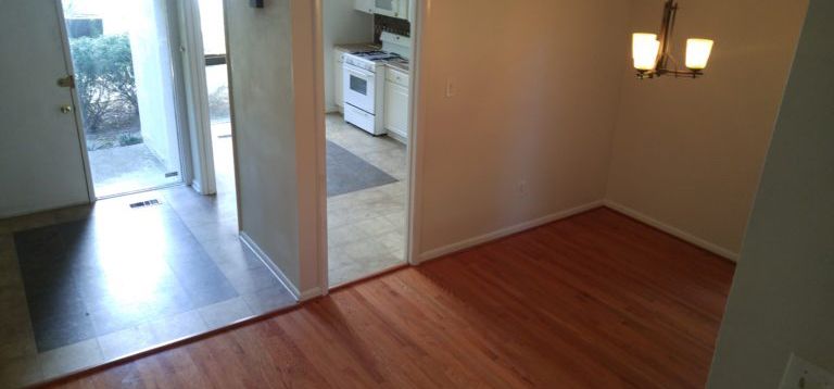 Interior view of a dining room with hardwood floors and a chandelier, with a doorway leading to the kitchen.