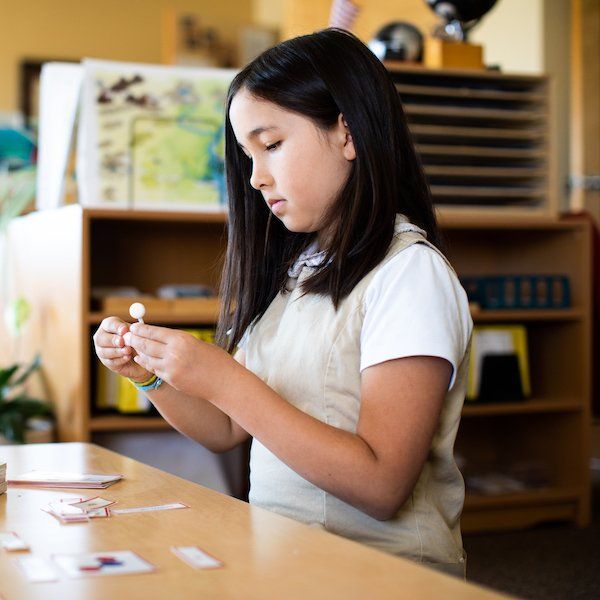 A young elementary girl is sitting at a table playing with a toy