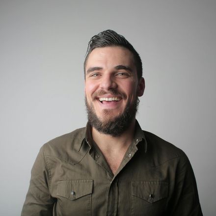 Man with dark beard and hair, smiling widely, wearing a green button-down shirt.