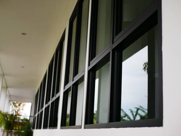 Black-framed windows on a white building exterior, reflecting the sky and greenery.