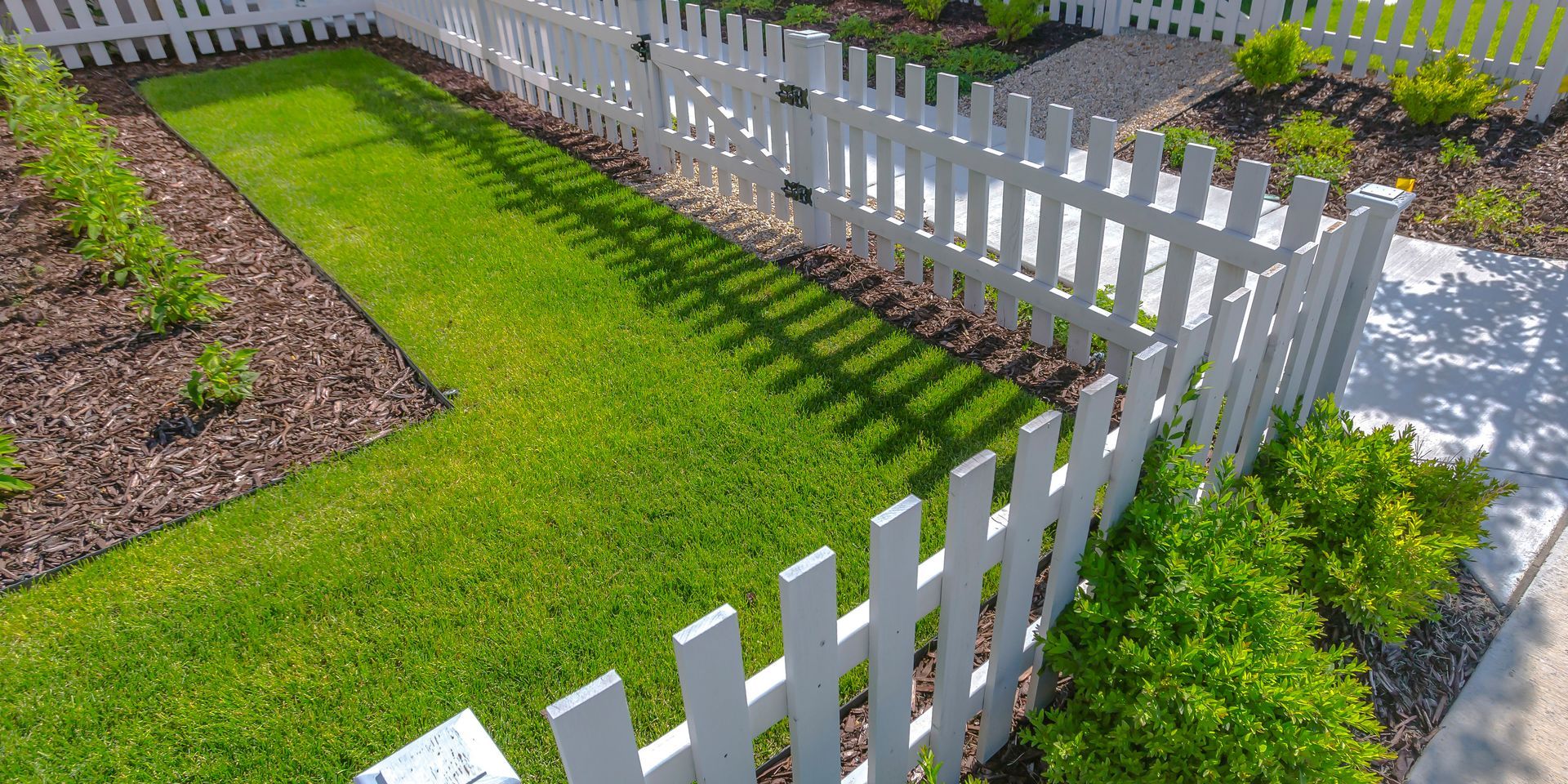 White picket fence surrounds a well-manicured lawn with a pathway and garden beds.