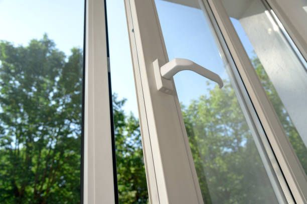 White casement window with open sash, handle visible. Trees and blue sky seen through the glass.