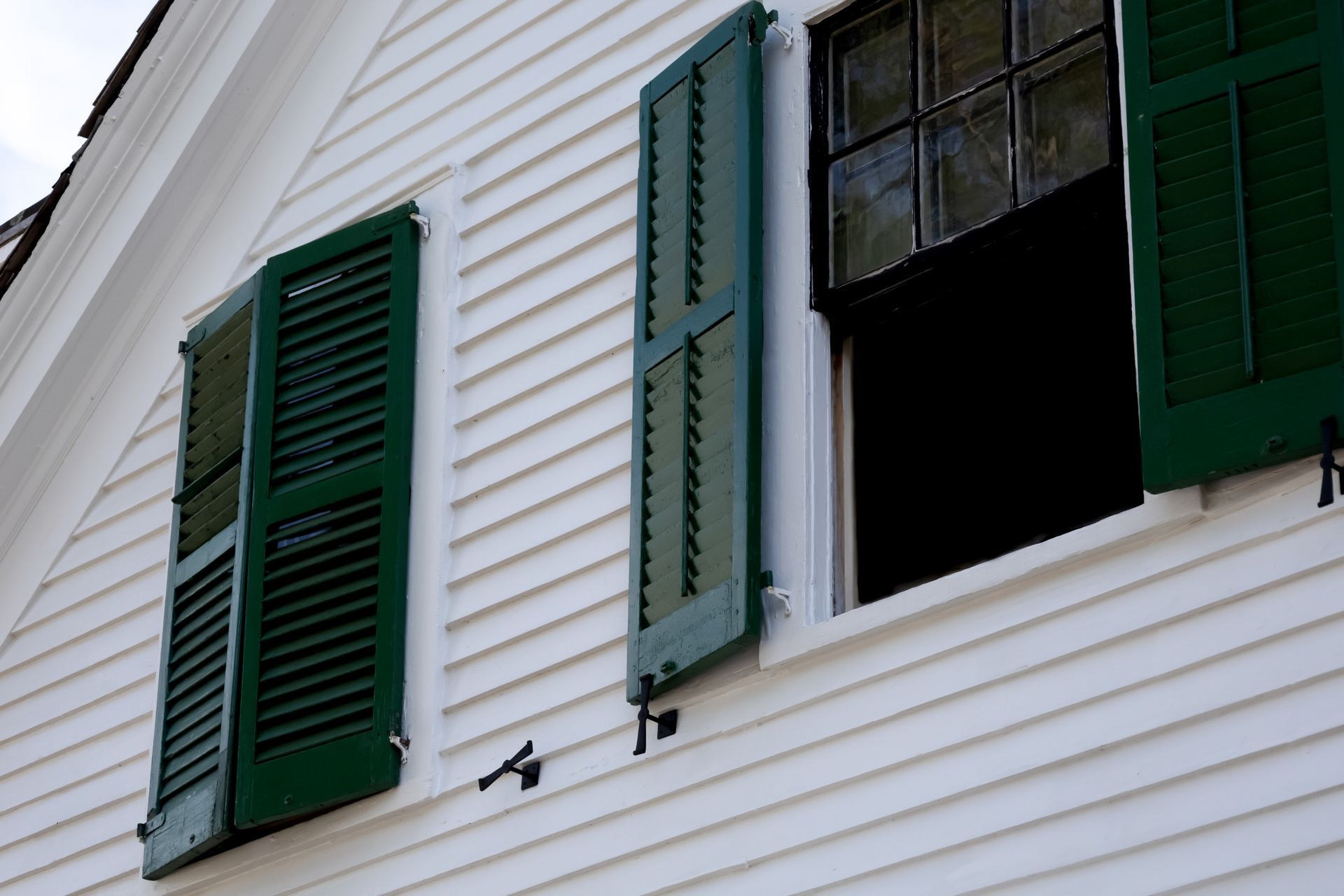 Man in blue shirt installing a black rain gutter on a white wall under a dark roof. Person in a blue shirt and hat installing a dark gutter on a white wall.
