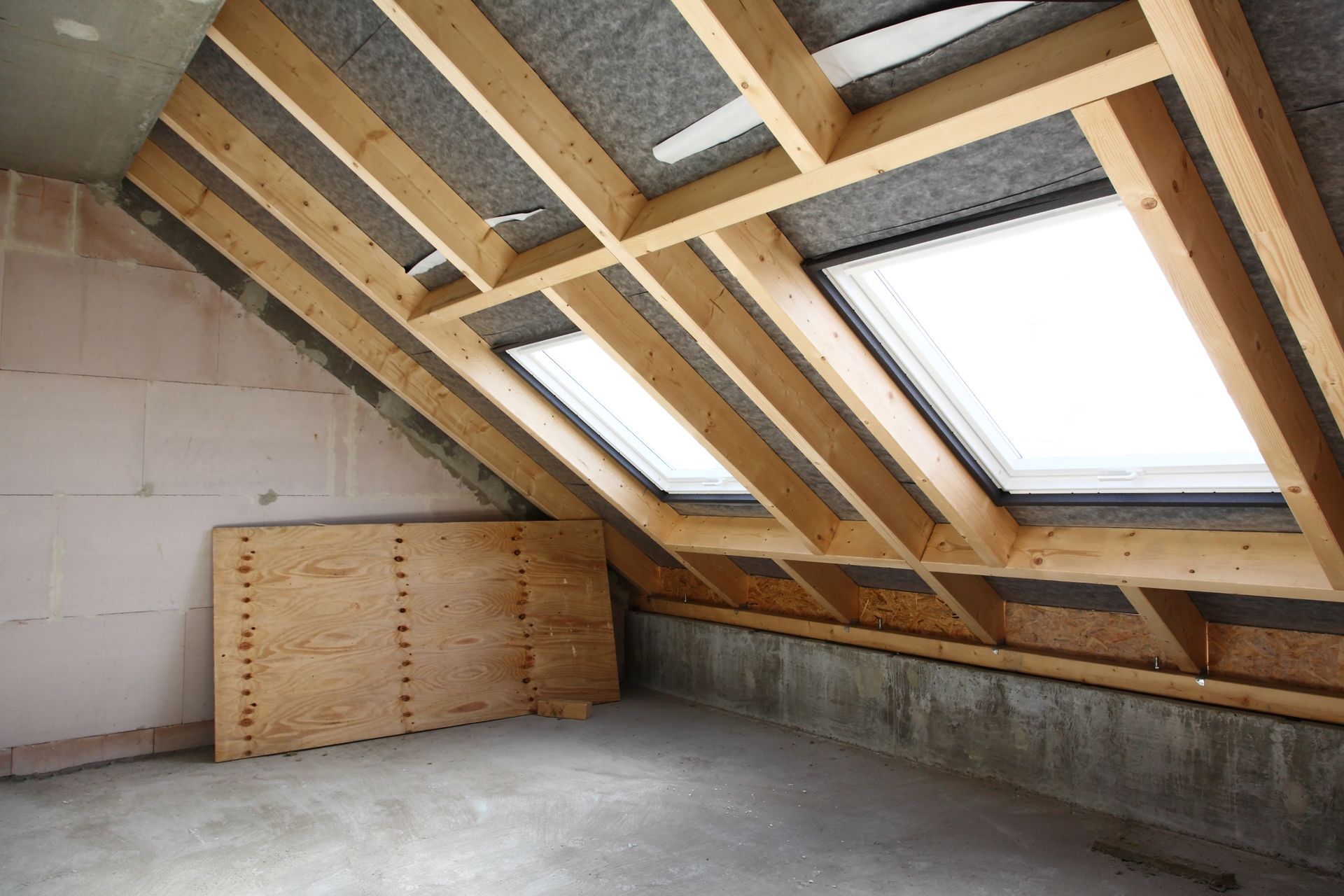 Interior of an unfinished attic with wooden framing, skylights, and concrete flooring.