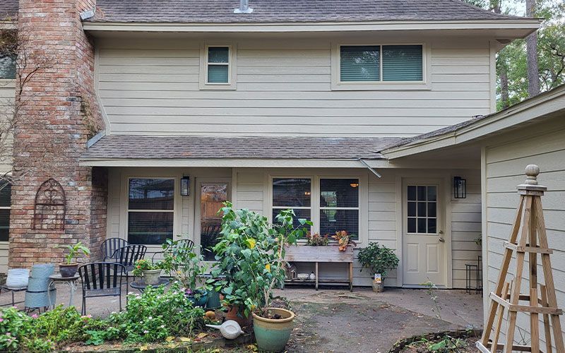 Beige house exterior with brick chimney, windows, and potted plants.