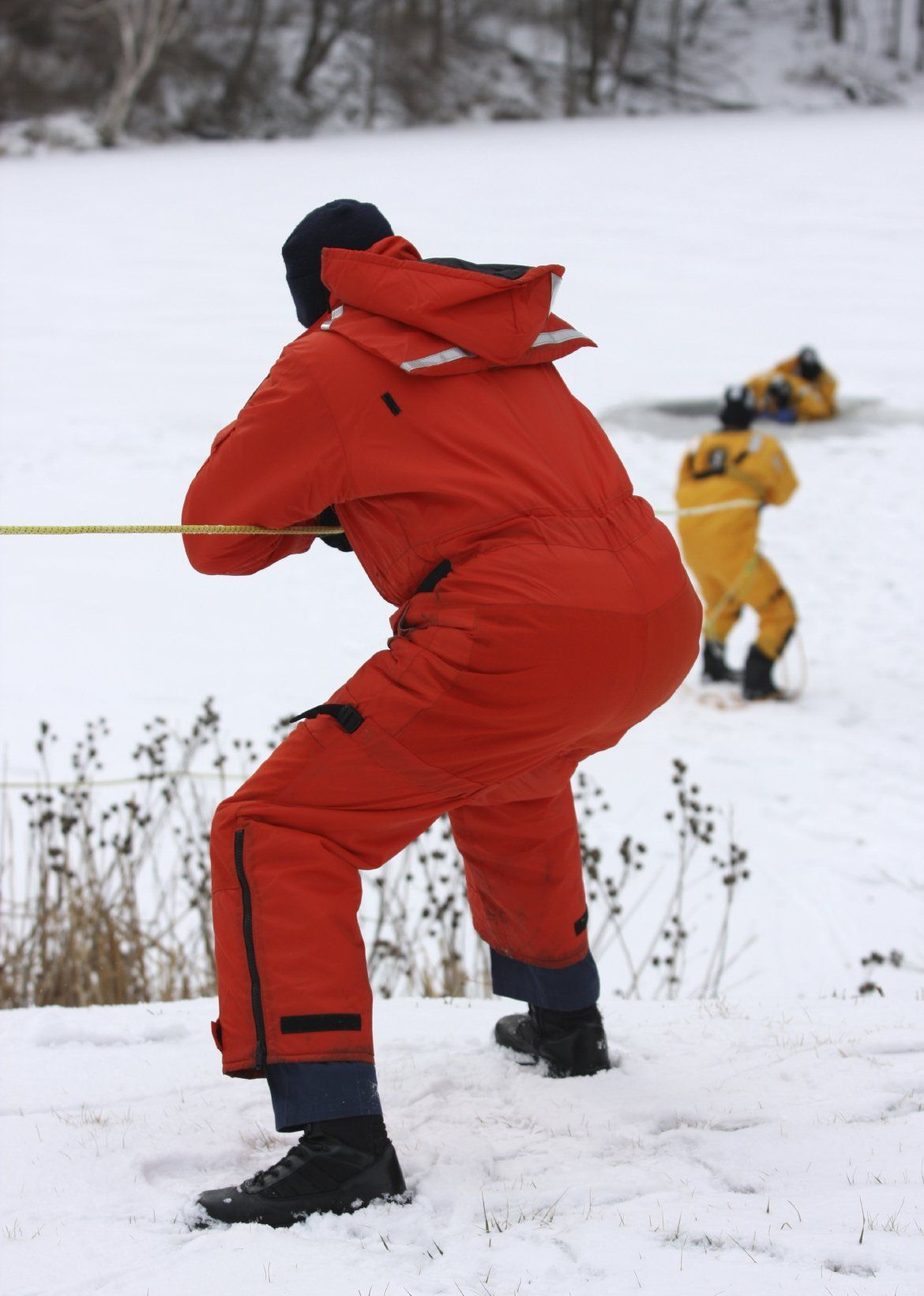 A man in a red suit is pulling a rope in the snow