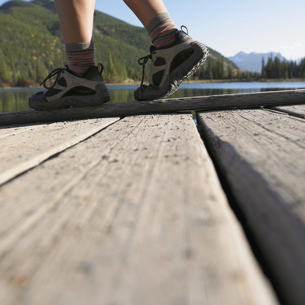 A person standing on a wooden dock with mountains in the background