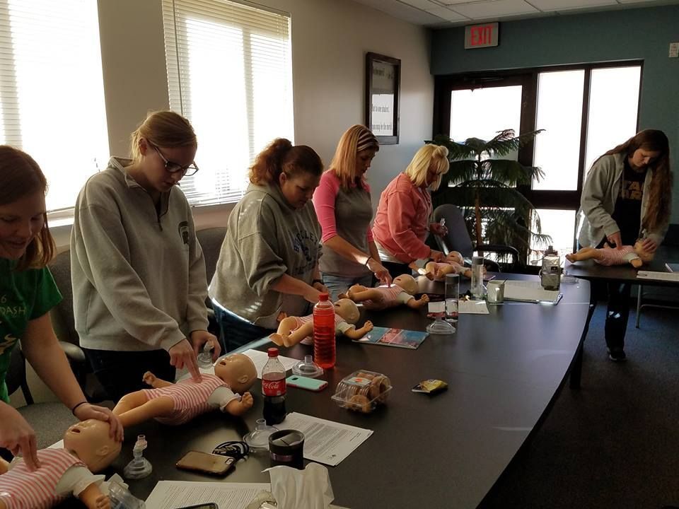 A group of women are sitting around a table with dolls on it.