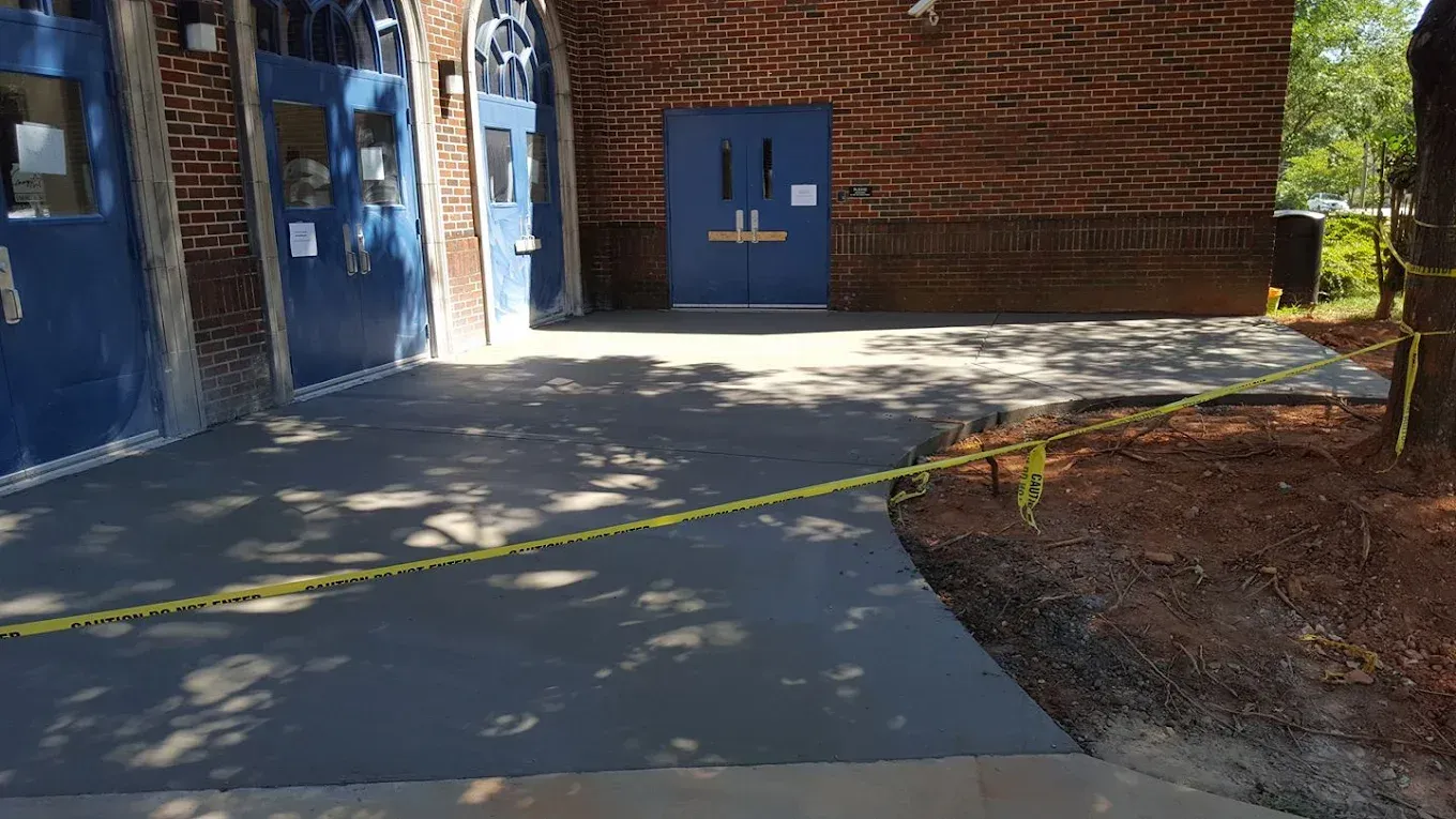 Newly poured concrete sidewalk and entrance to a blue-doored building, caution tape in the foreground.