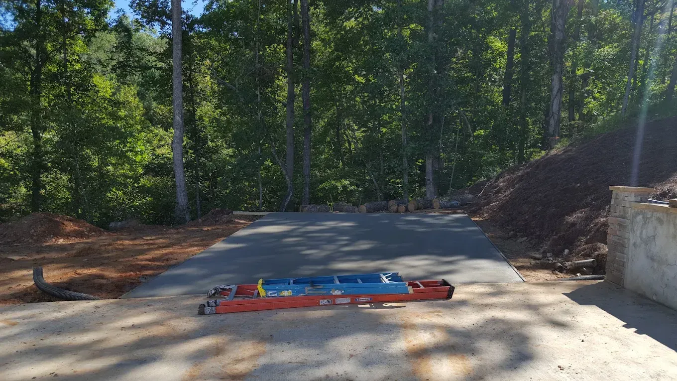 A blue and red cylindrical object on a trailer sits on a concrete pad in front of a forested area.