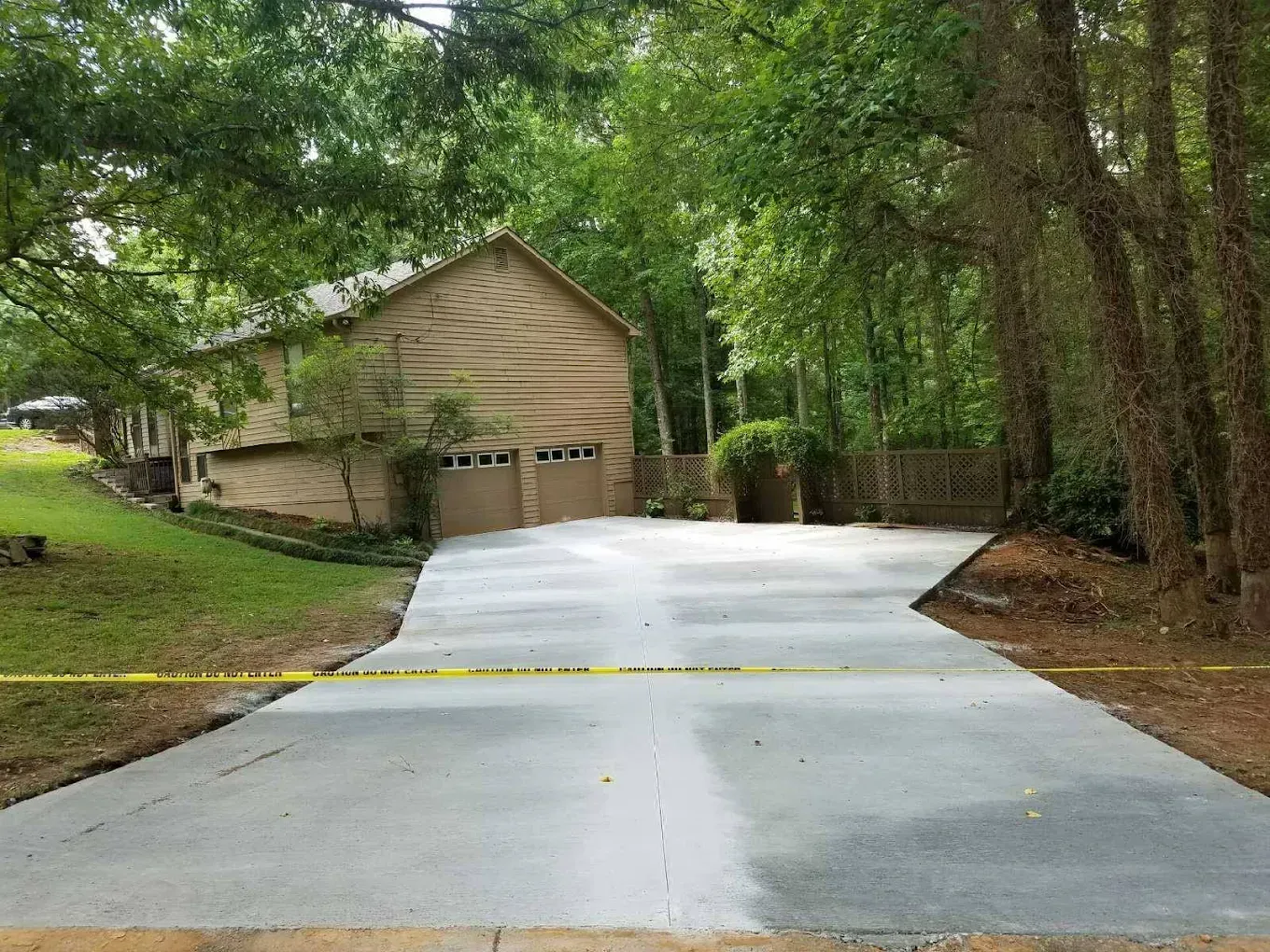 Newly poured concrete driveway leading to a two-story house with a garage; surrounded by trees.