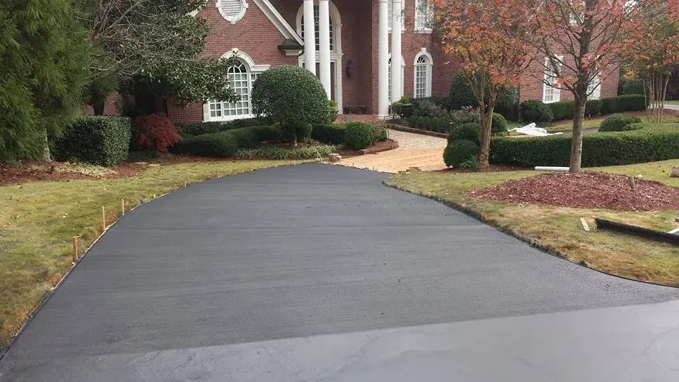 Newly paved dark gray driveway leading to a brick house with landscaping.