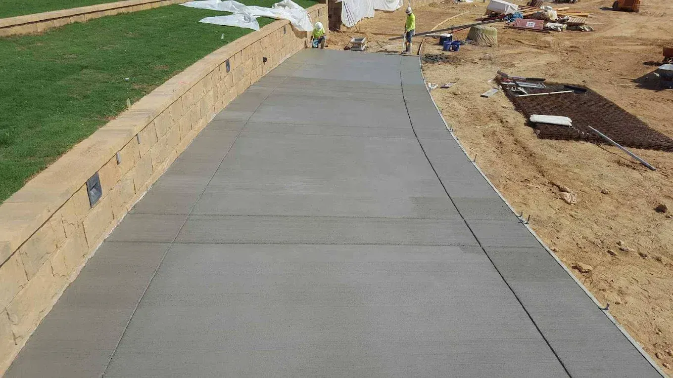 Newly poured concrete driveway with retaining wall and construction workers.