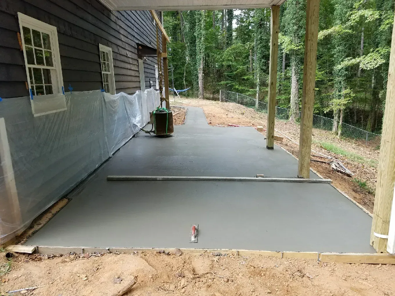 Newly poured concrete patio next to a dark wood house, under a covered porch.