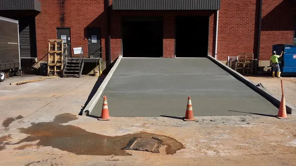 A newly built concrete loading dock ramp with safety cones in front of a brick warehouse.