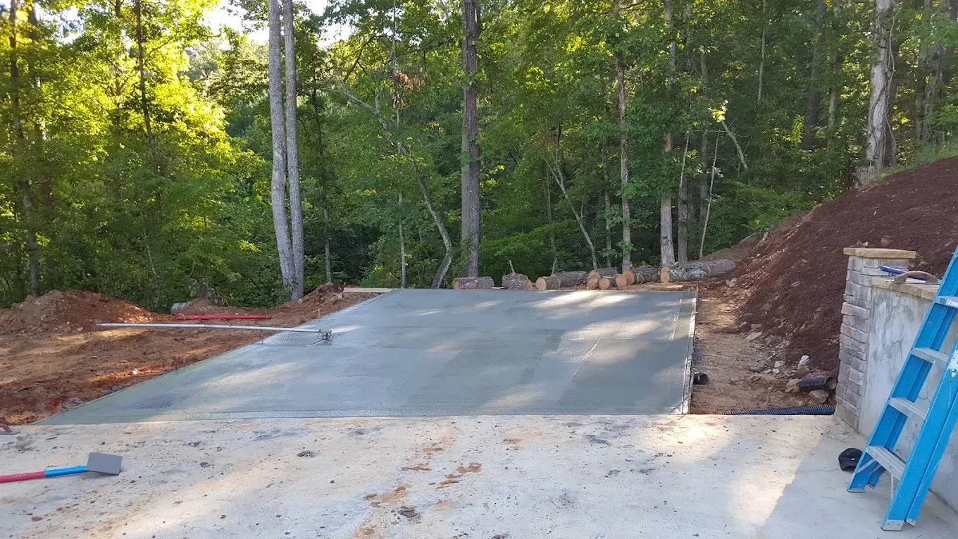 A concrete slab, likely a patio, is being built outdoors; the backdrop is a wooded hillside.