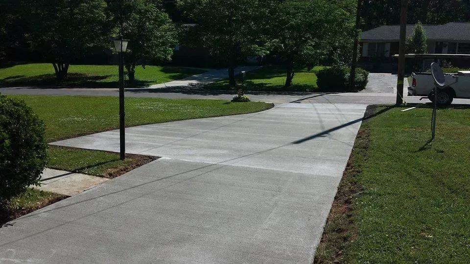 Concrete driveway leading to a residential street with a lamp post and truck. Green grass surrounds.