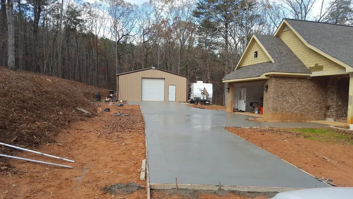 A new concrete driveway leading to a house and detached garage on a wooded property.