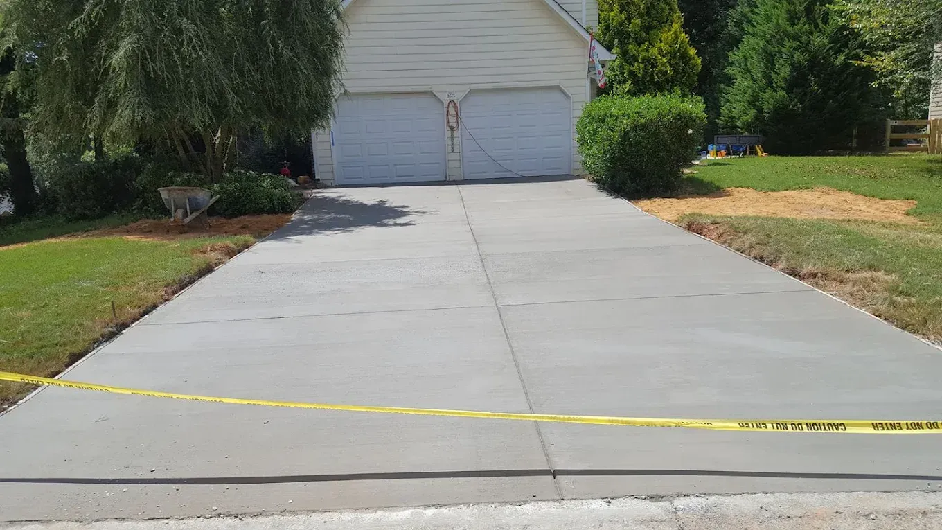 Freshly poured concrete driveway with yellow caution tape in front of a two-car garage.