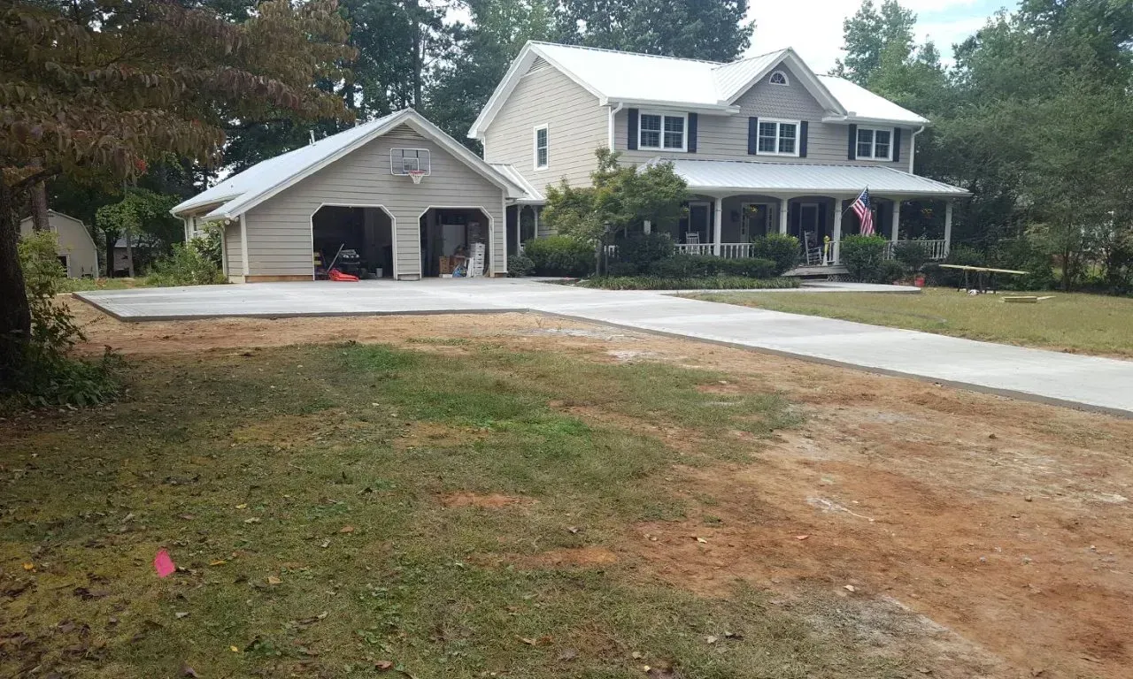 House with two-car garage and long driveway. Beige siding, white roof, surrounded by trees and yard.