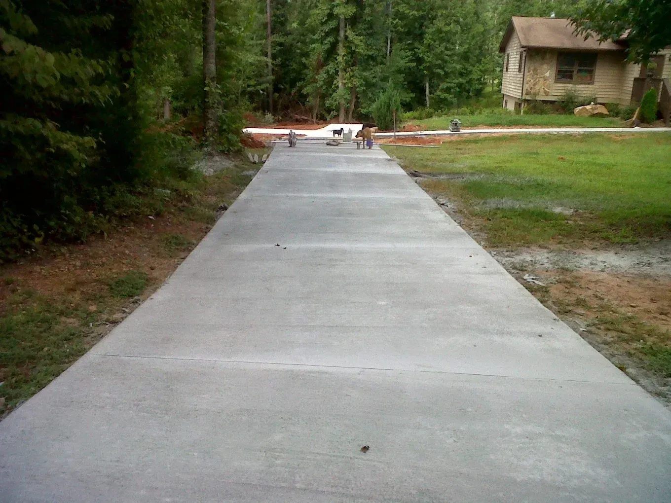 Newly poured concrete driveway leading to a house in a wooded area.