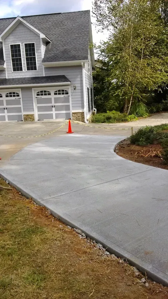 Newly poured concrete driveway curves toward a light gray two-story house with a three-car garage.