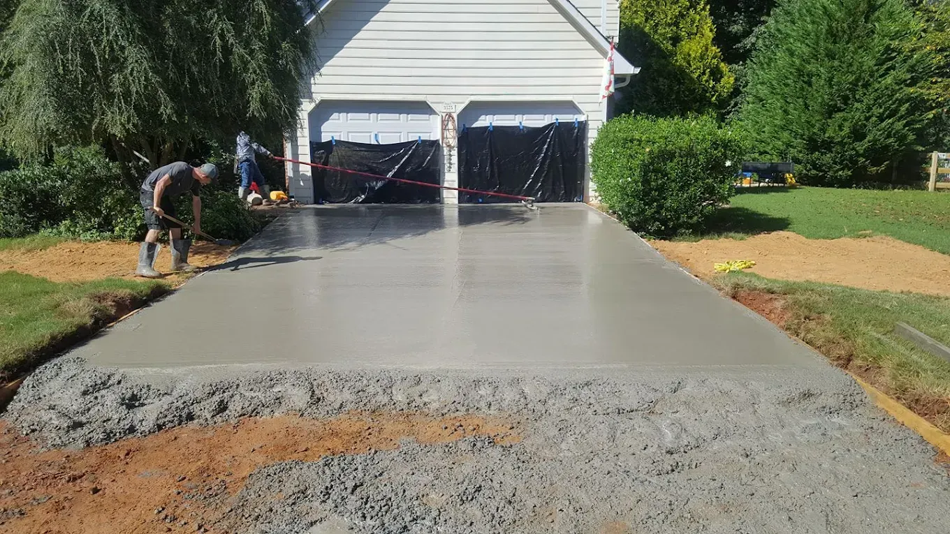 A man smoothing wet concrete on a driveway in front of a house with two garage doors.
