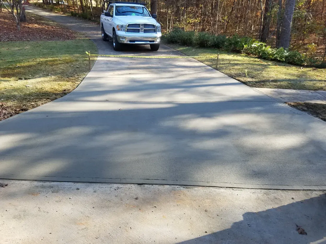 White pickup truck parked on a gray concrete driveway, surrounded by grass and trees.