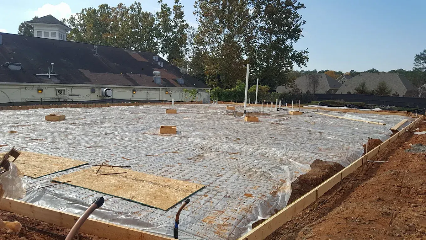 Construction site with concrete foundation prepped for pouring. Wooden forms and pipes are visible.