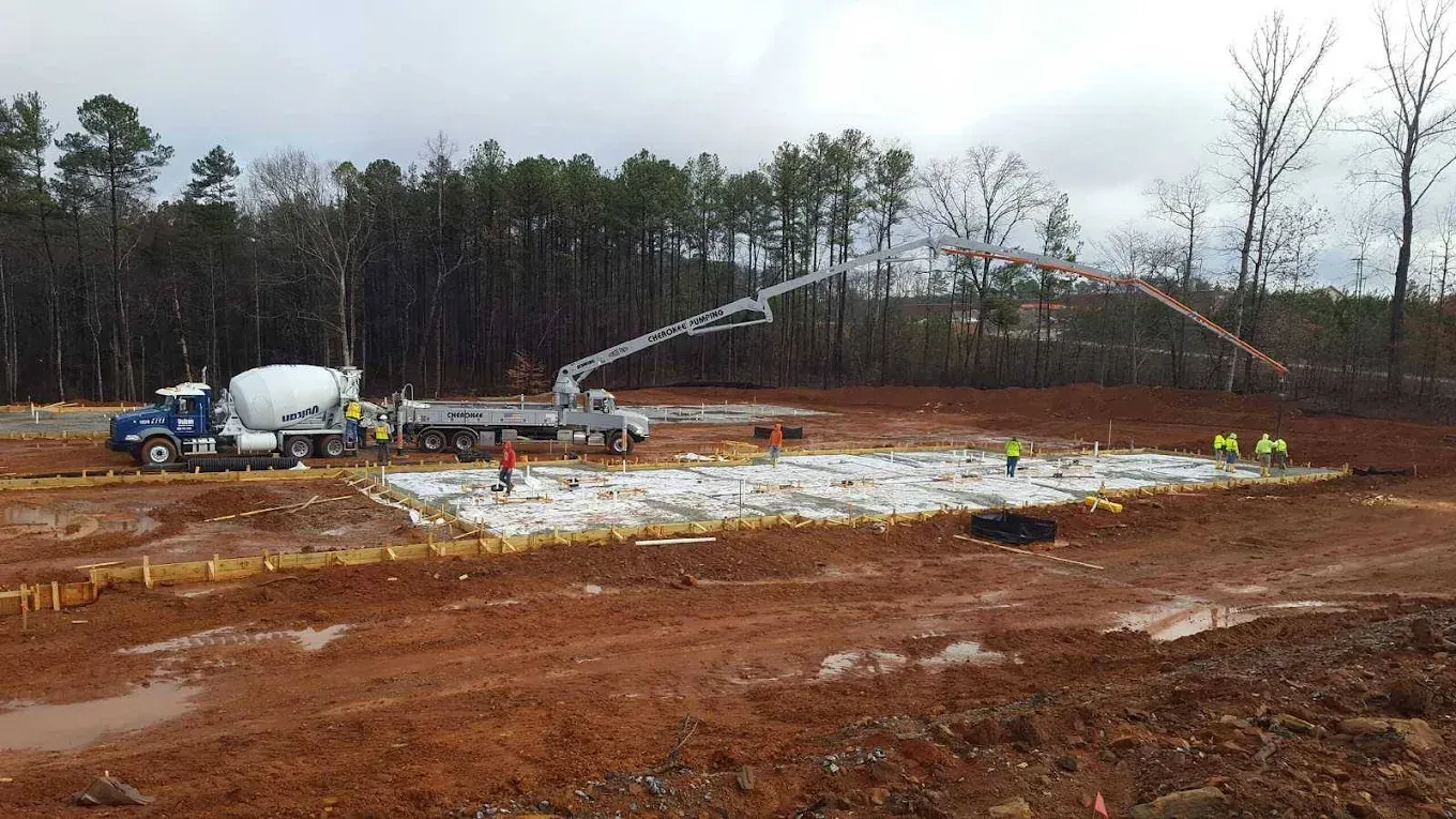 Concrete being poured at a construction site; truck, boom, workers, and muddy ground.