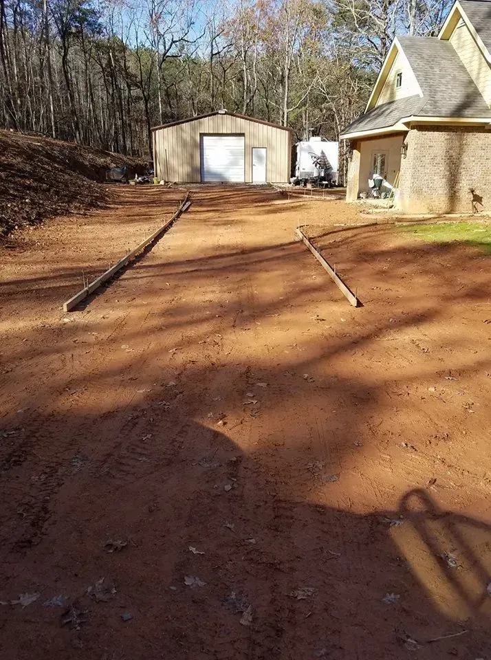 Dirt driveway with wooden posts, shed, house, and trees.