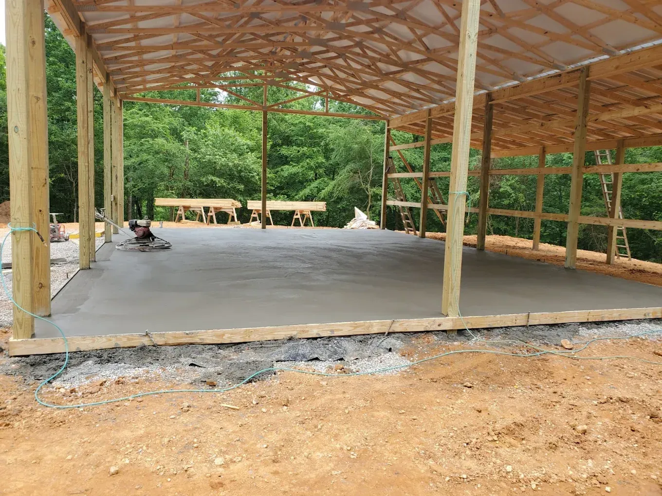 Concrete floor poured inside a partially built wooden barn frame; setting is outdoors.