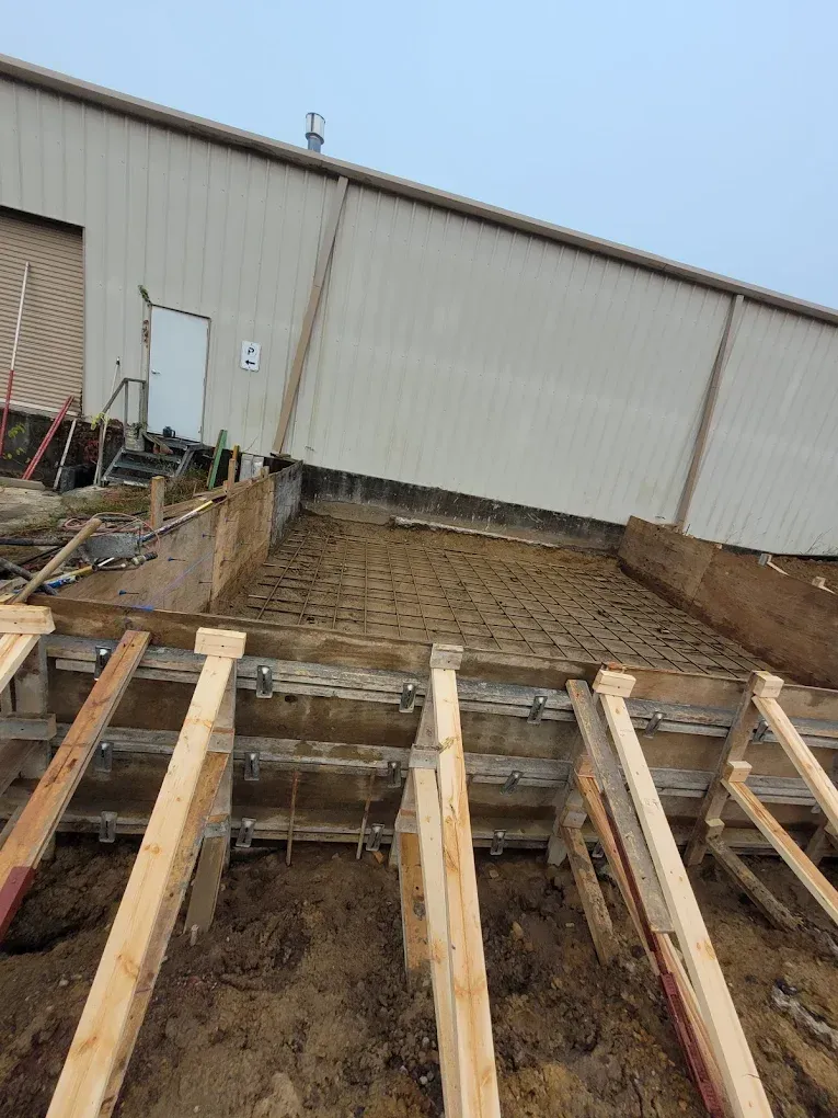 Construction site with wooden forms and rebar, preparing to pour concrete next to a building.