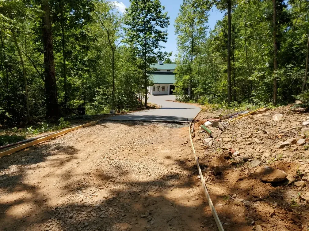 Gravel driveway leads to a building amidst trees, with green roof visible. Sunny day.