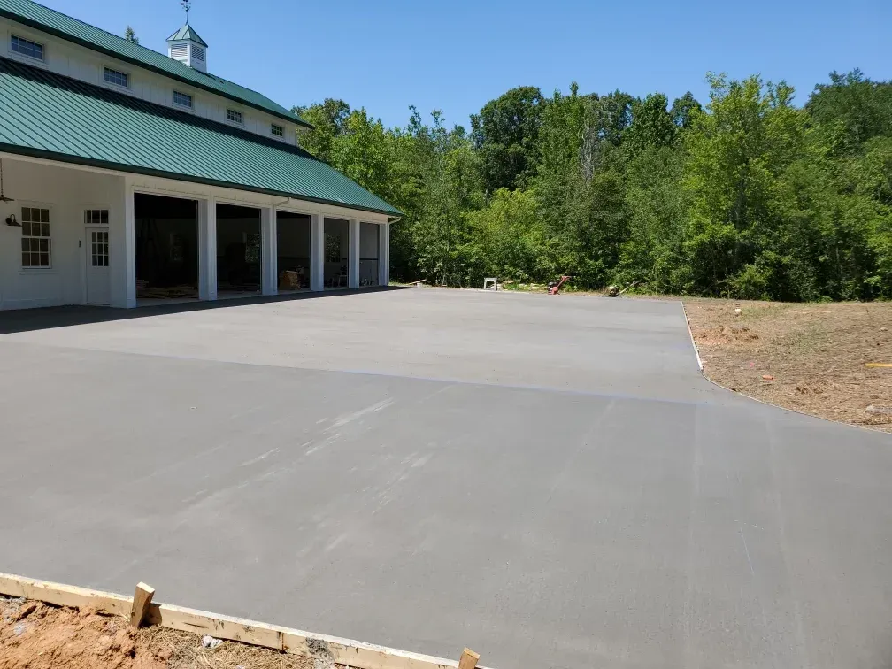 A newly poured concrete driveway in front of a white building with a green roof, trees in the background.