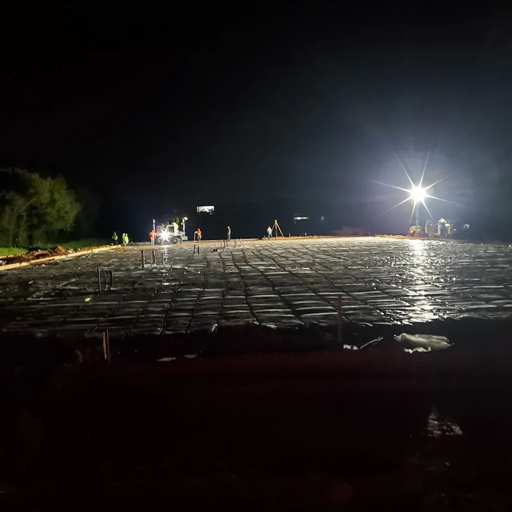 Night construction site with workers and equipment preparing to pour concrete.