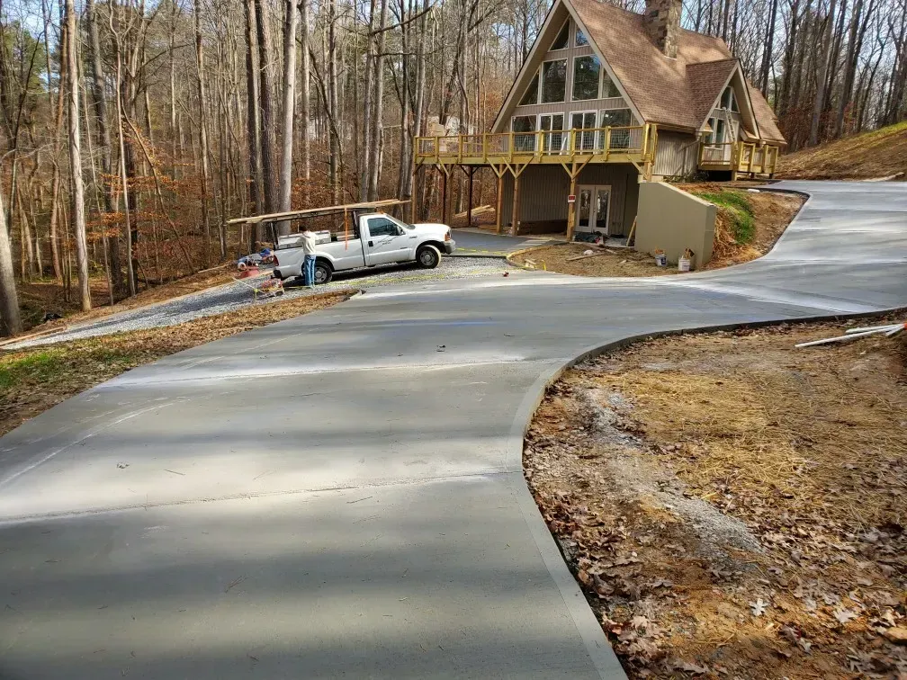 A light-colored concrete driveway curves towards a cabin-style house with a pickup truck parked nearby.