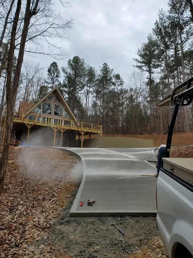 Driveway being sprayed with water, near a cabin in the woods.