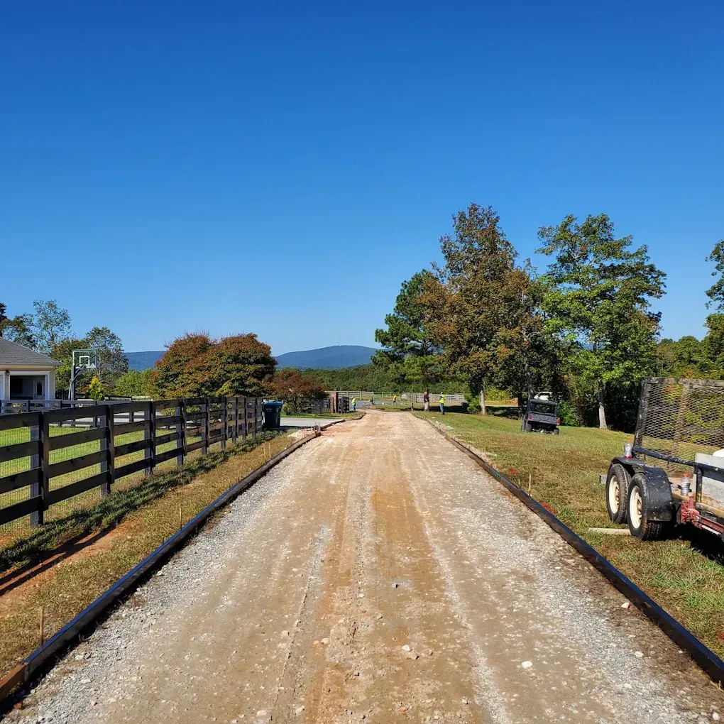 Gravel driveway with black edging, flanked by grass and a wooden fence under a clear blue sky.