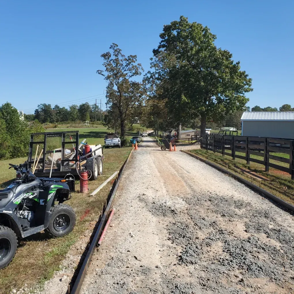 Construction site: A gravel road under repair with machinery, fencing, and workers on a sunny day.