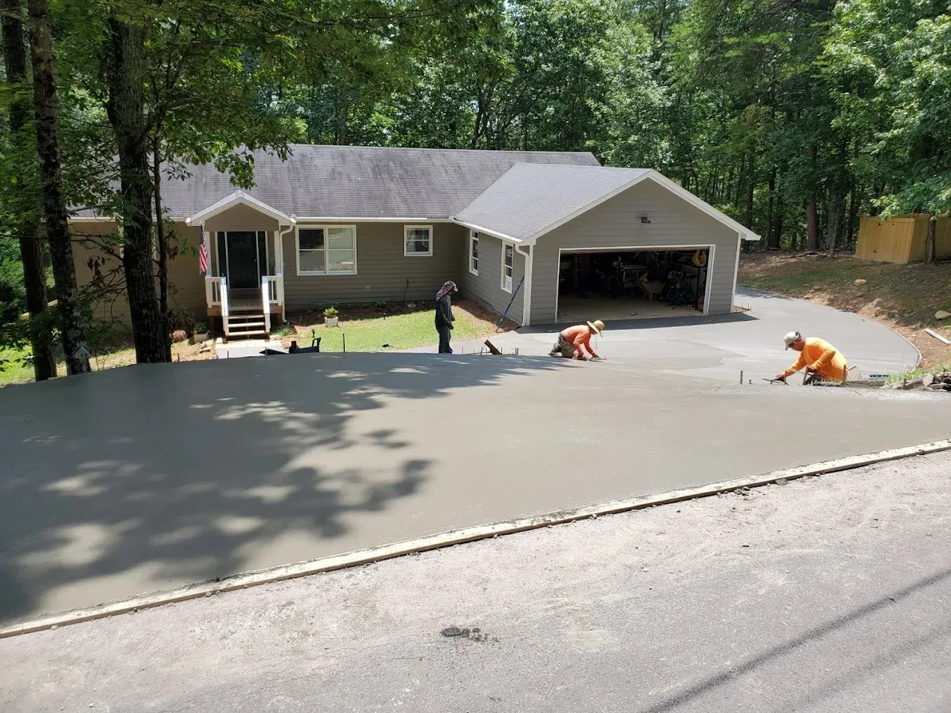 Workers paving a gray concrete driveway in front of a beige house with a two-car garage.