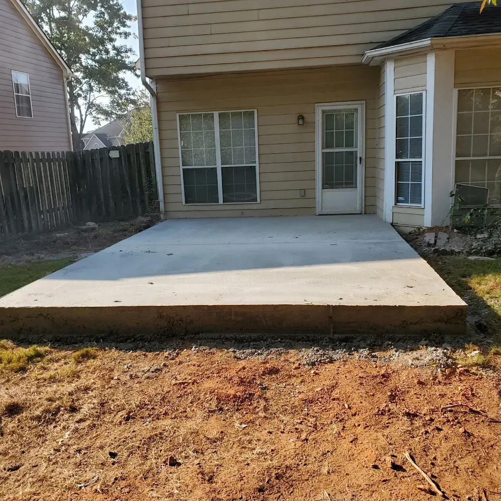 Concrete patio outside a house with a door and windows; dirt and grass surround it.